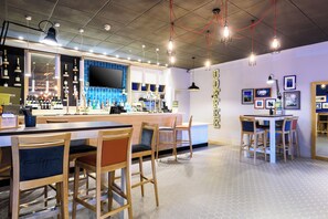 A bar area with wooden chairs, a counter with bottles, and a large TV screen. - Holiday Inn Portsmouth by IHG (Portsmouth)
