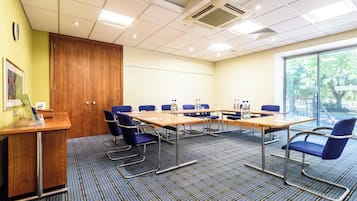 Un salón de conferencias con una mesa larga, sillas azules y un escritorio de madera con una computadora.