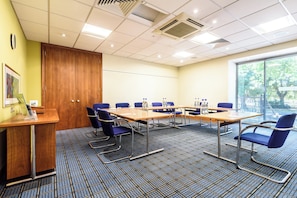 A conference room with a long table, blue chairs, and a wooden desk with a computer. - Holiday Inn Portsmouth by IHG (Portsmouth)