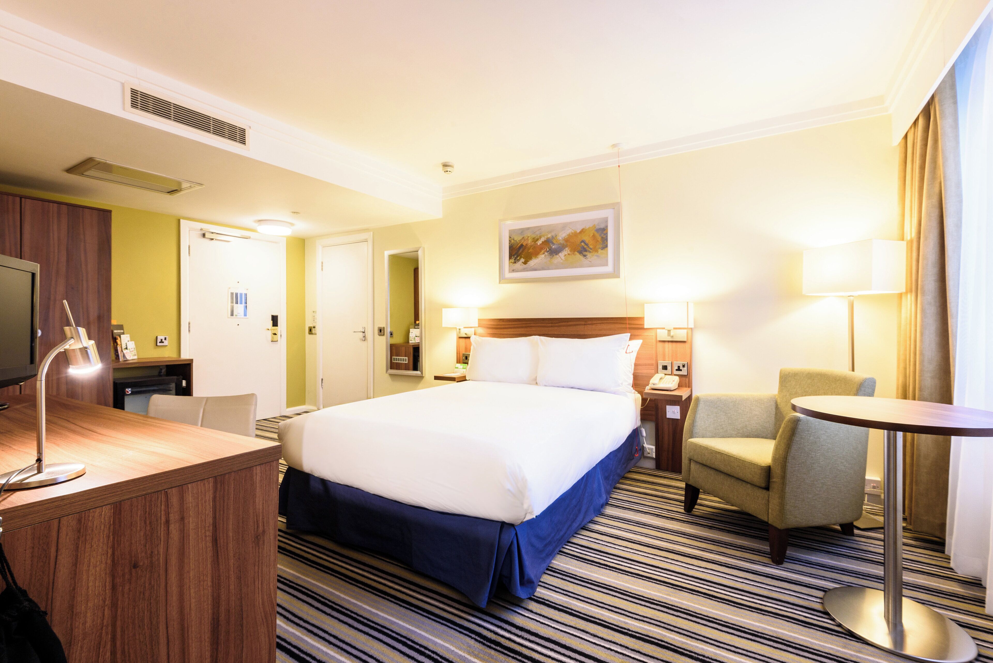 A hotel room with a bed, desk, chair, and a small table.
