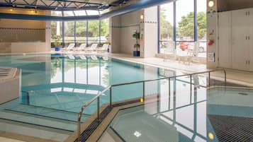 An indoor swimming pool with clear water, a diving board, and lounge chairs.