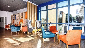 A modern lounge area with wooden panel dividers, a variety of seating options including armchairs and sofas, and large windows offering a view of the outside. - Holiday Inn Portsmouth by IHG (Portsmouth)