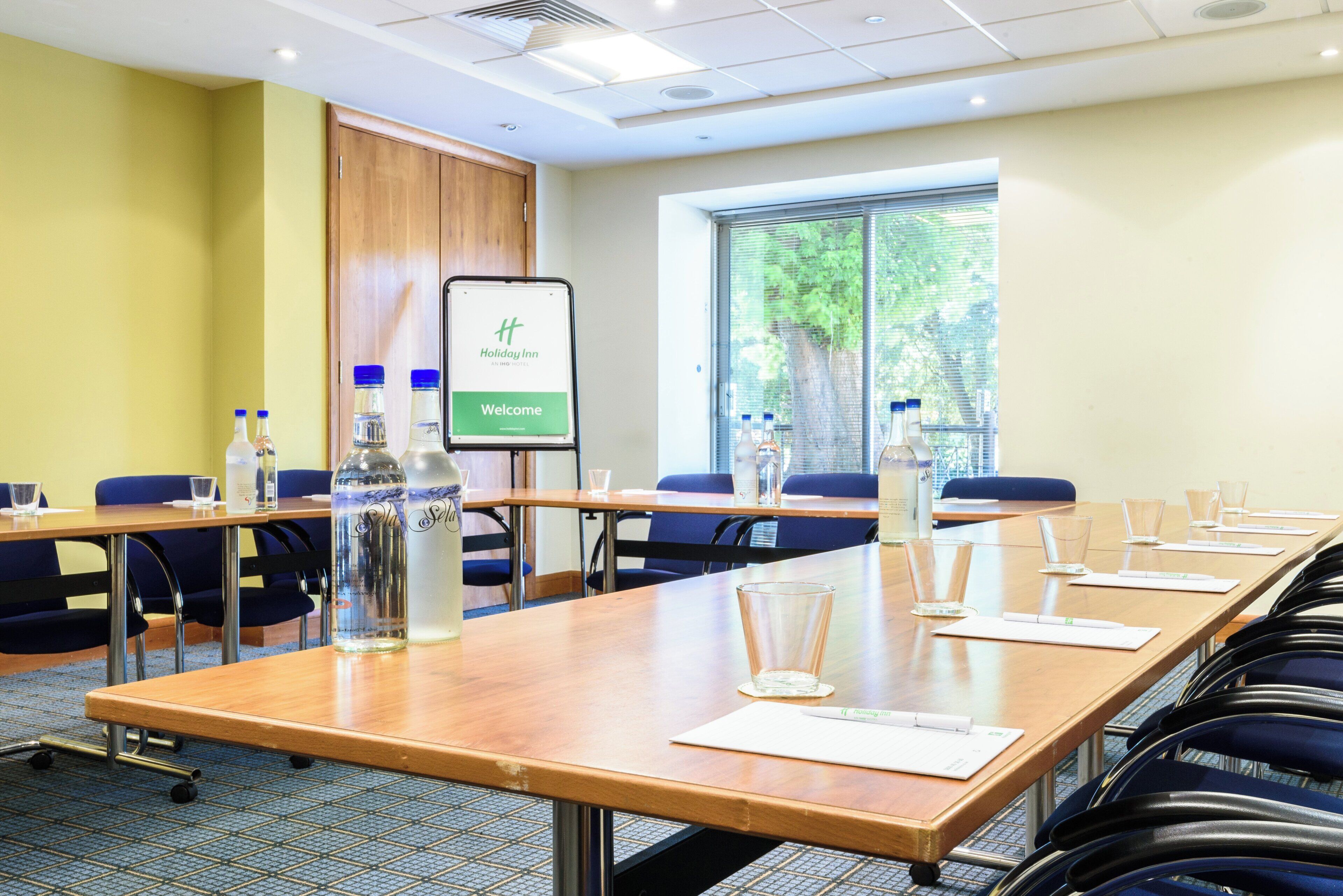 A conference room with a long table, chairs, water bottles, and a presentation screen displaying 'Holiday Inn.'