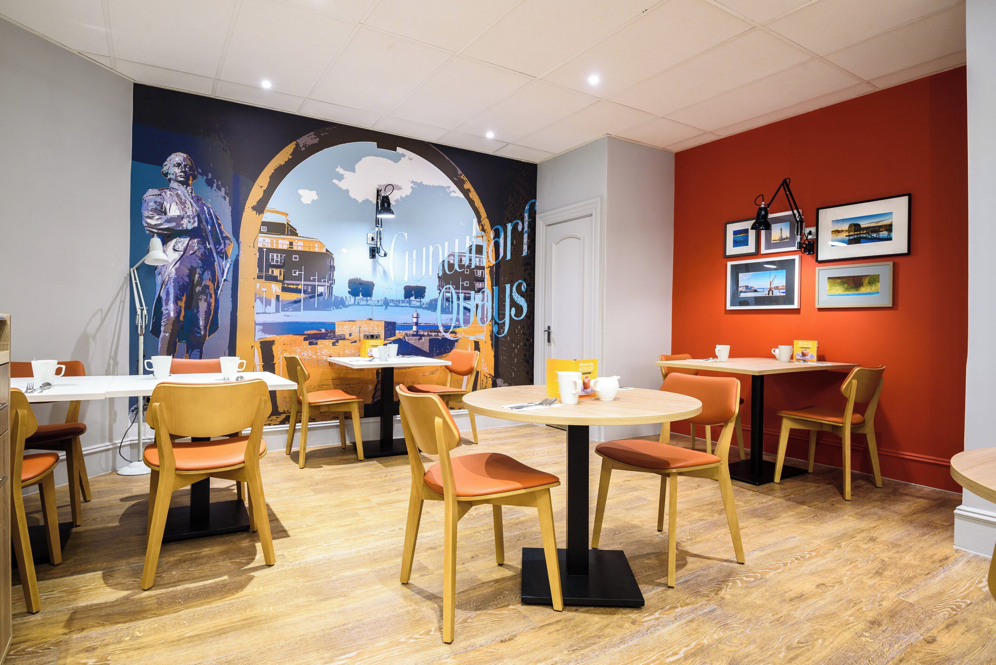 Un restaurant amb taules i cadires rodones, un mural a la paret i quadres emmarcades a la paret.