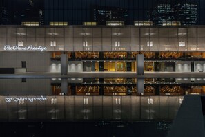 A modern building with a reflective glass facade, 'The Okura Prestige' signage, and multiple levels with interior lighting. - Hotel Okura Tokyo South Wing (Tokyo)