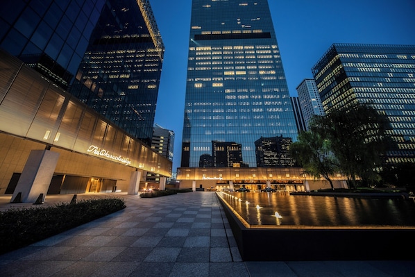 A modern hotel with a glass facade, a spacious courtyard, and a well-lit entrance.