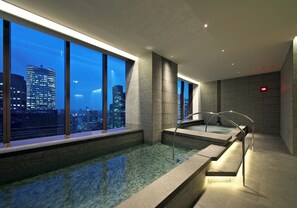 A modern indoor pool with a city view, a glass barrier, and a red exit sign. - Hotel Okura Tokyo South Wing (Tokyo)