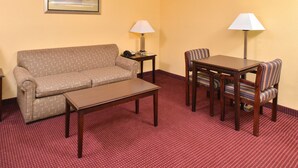 A hotel room with a sofa, a small table, a dining table with chairs, two lamps, and a framed picture on the wall.