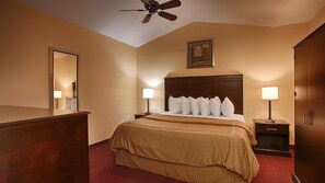 A hotel room with a large bed, two bedside tables with lamps, a wooden headboard, a ceiling fan, a framed picture on the wall, and a red carpeted floor. - Americas Best Value Inn Winnsboro, LA (Winnsboro)