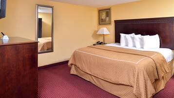 A hotel room with a large bed, a wooden dresser, a mirror, a bedside lamp, and a framed picture on the wall.