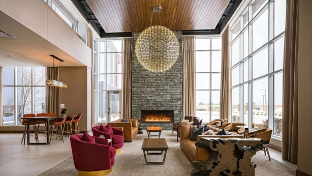 A spacious living room with a fireplace, large windows, and modern furniture. - Hilton Garden Inn Wausau (Wausau)