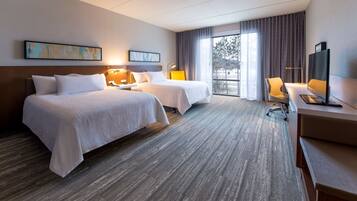 Habitación de hotel con dos camas, un escritorio, una silla y un ventanal con cortinas.