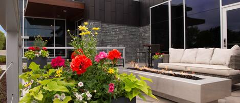 Un espacio de estar moderno al aire libre con una chimenea integrada, rodeado de coloridos maceteros con flores.