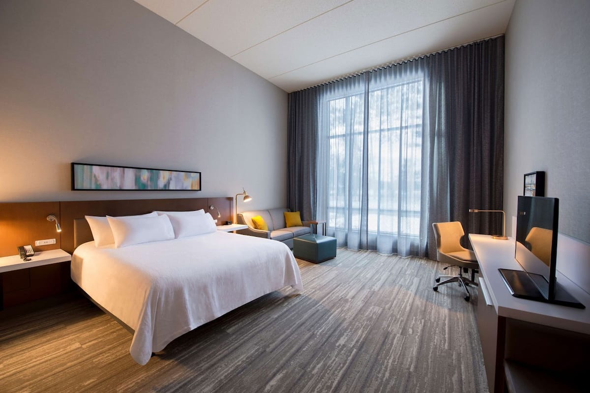 Une chambre d’hôtel avec un grand lit, un bureau avec une chaise, un canapé, une télévision et une fenêtre avec des rideaux.