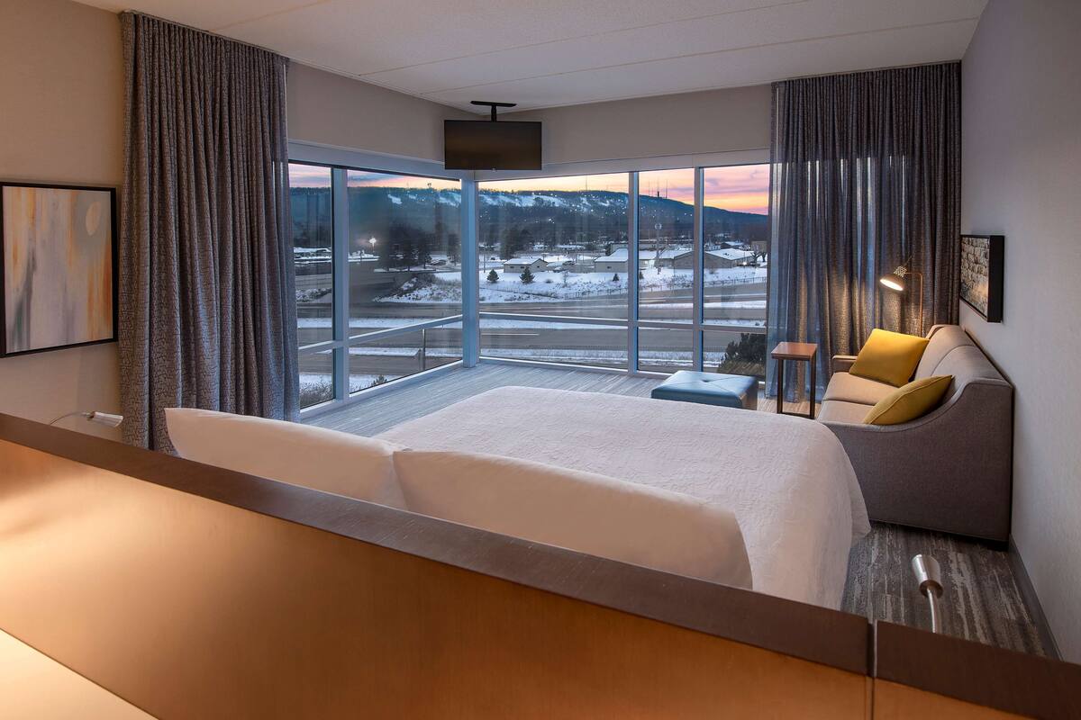 Une chambre d’hôtel avec un grand lit, un canapé, un bureau et une vue sur un paysage enneigé.