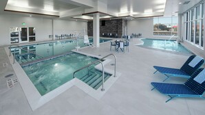 A modern indoor pool area with two pools, lounge chairs, and a seating area with tables and chairs. - Hilton Garden Inn Wausau (Wausau)