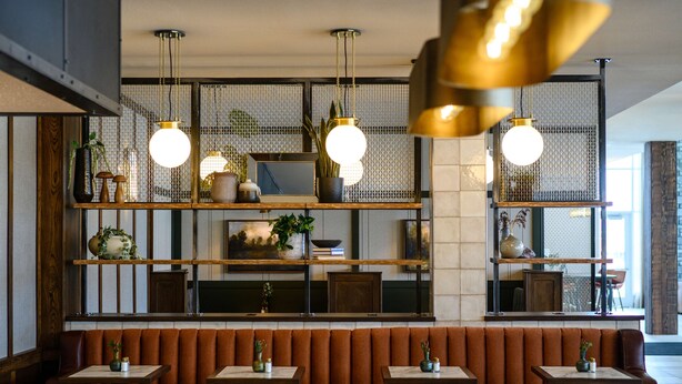 A restaurant interior with booths, tables, hanging pendant lights, and shelves with decorative items. - Hilton Garden Inn Wausau (Wausau)