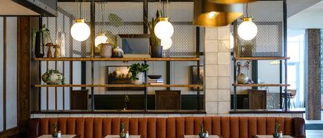 L’intérieur d’un restaurant, avec des banquettes, des tables, des suspensions décoratives et des étagères ornées d’objets décoratifs.