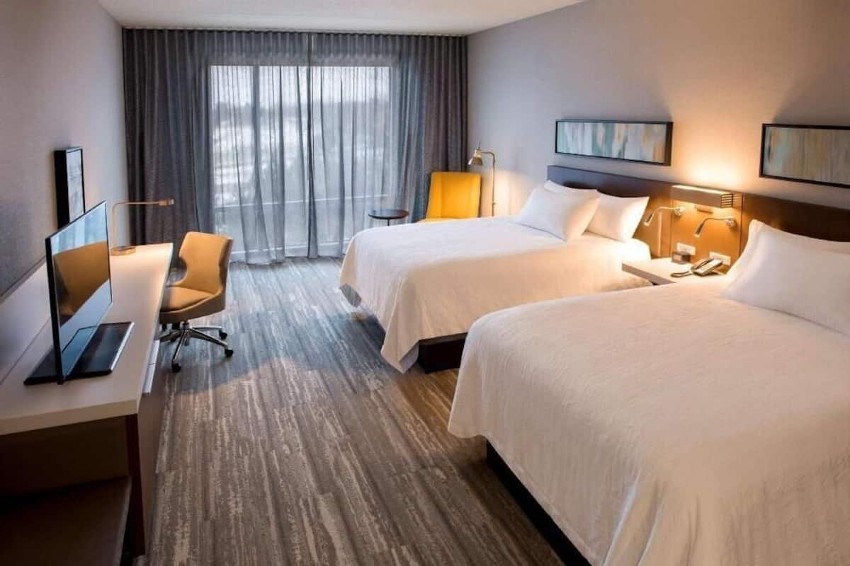 Une chambre d’hôtel avec deux lits, un bureau avec un ordinateur, une chaise et une fenêtre avec des rideaux.