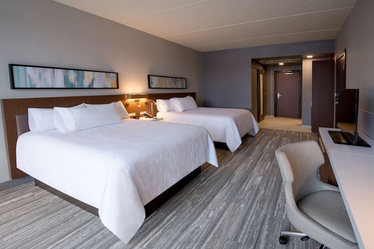Une chambre d’hôtel avec deux lits, un bureau, une chaise et un téléviseur.