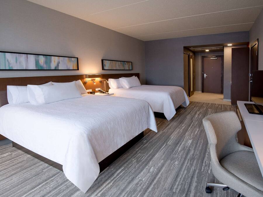A hotel room with two beds, a desk, a chair, and a TV.
