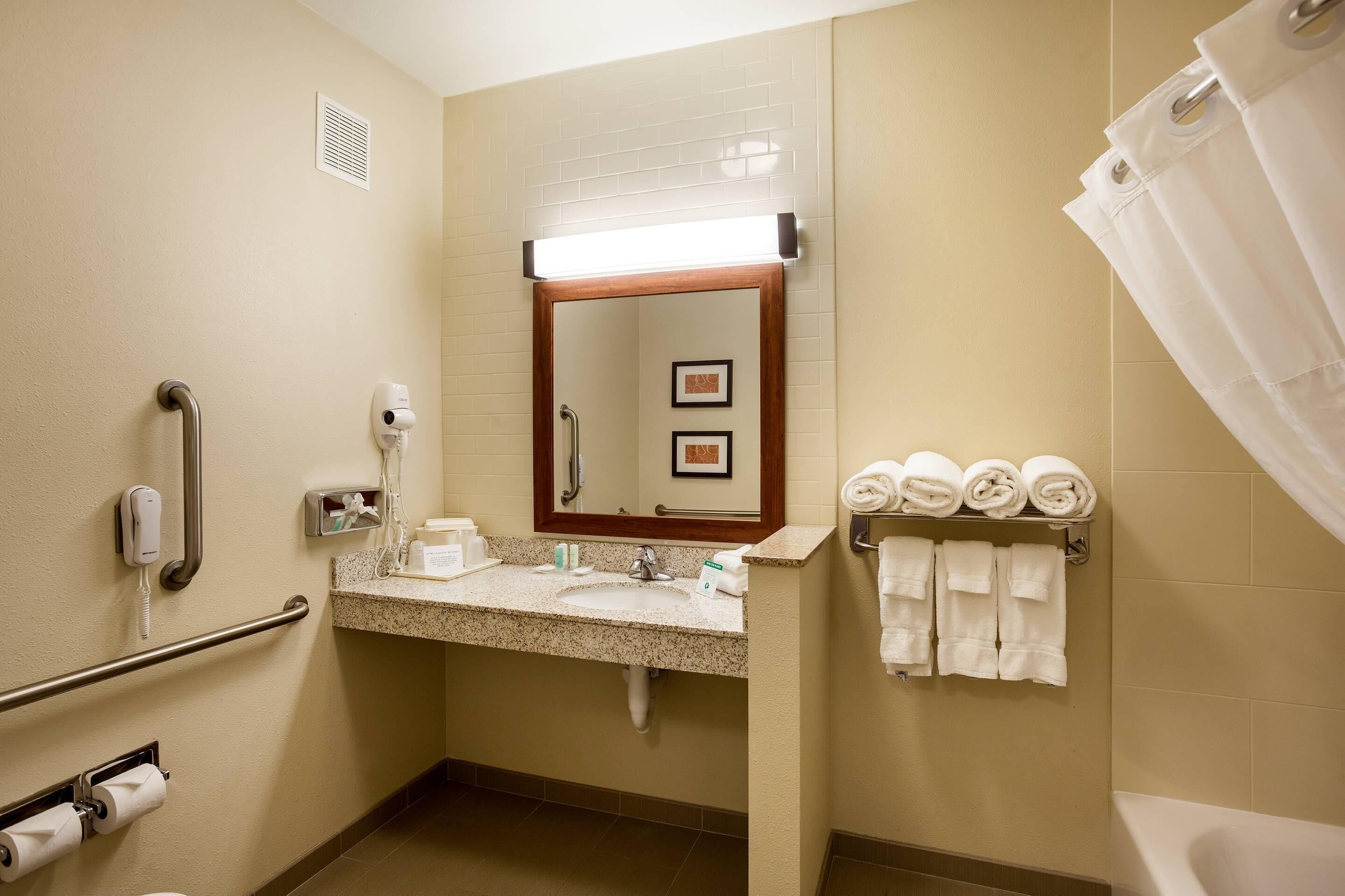 A hotel bathroom with a sink, mirror, towel rack, and a shower curtain.