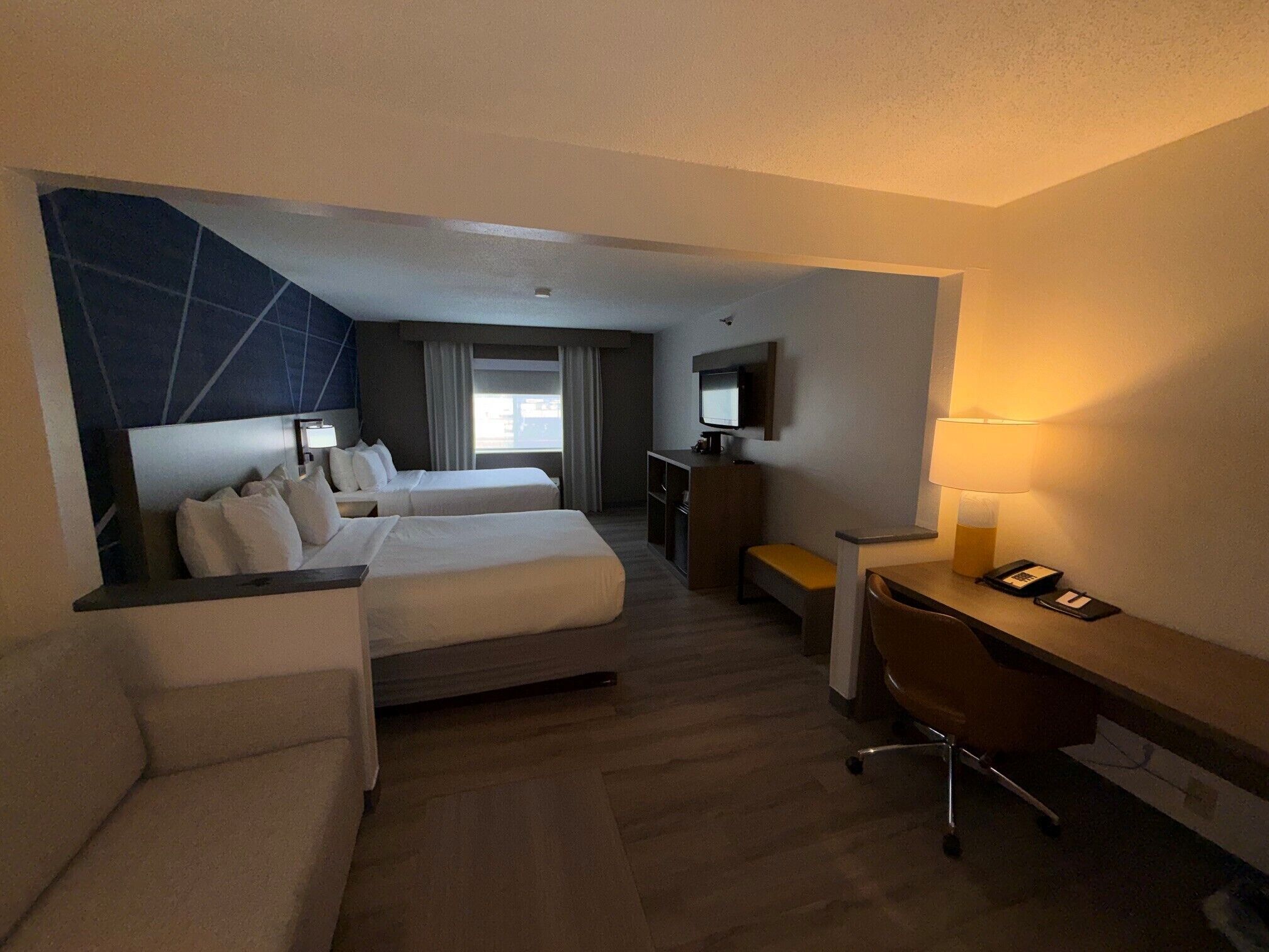 A hotel room with a bed, a desk, a chair, a TV, and a window.