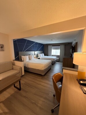 Ein Hotelzimmer mit Bett, Sofa, Schreibtisch mit Lampe und Fernseher.