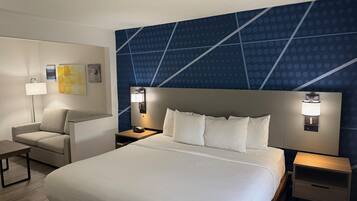 Una habitación de hotel con una cama grande, dos mesitas de noche con lámparas, un sofá y una pared con diseño geométrico.