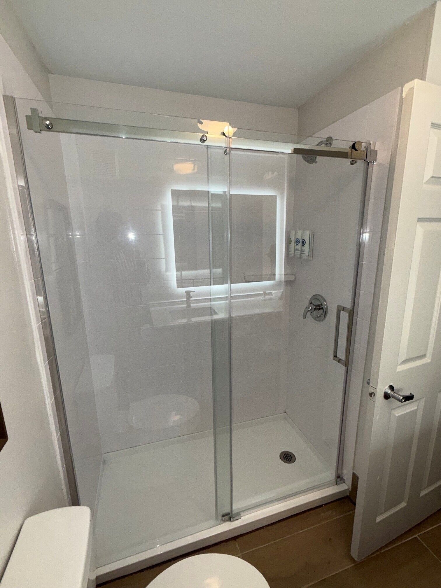 A glass-enclosed shower stall with a door, a white toilet, and a white door.