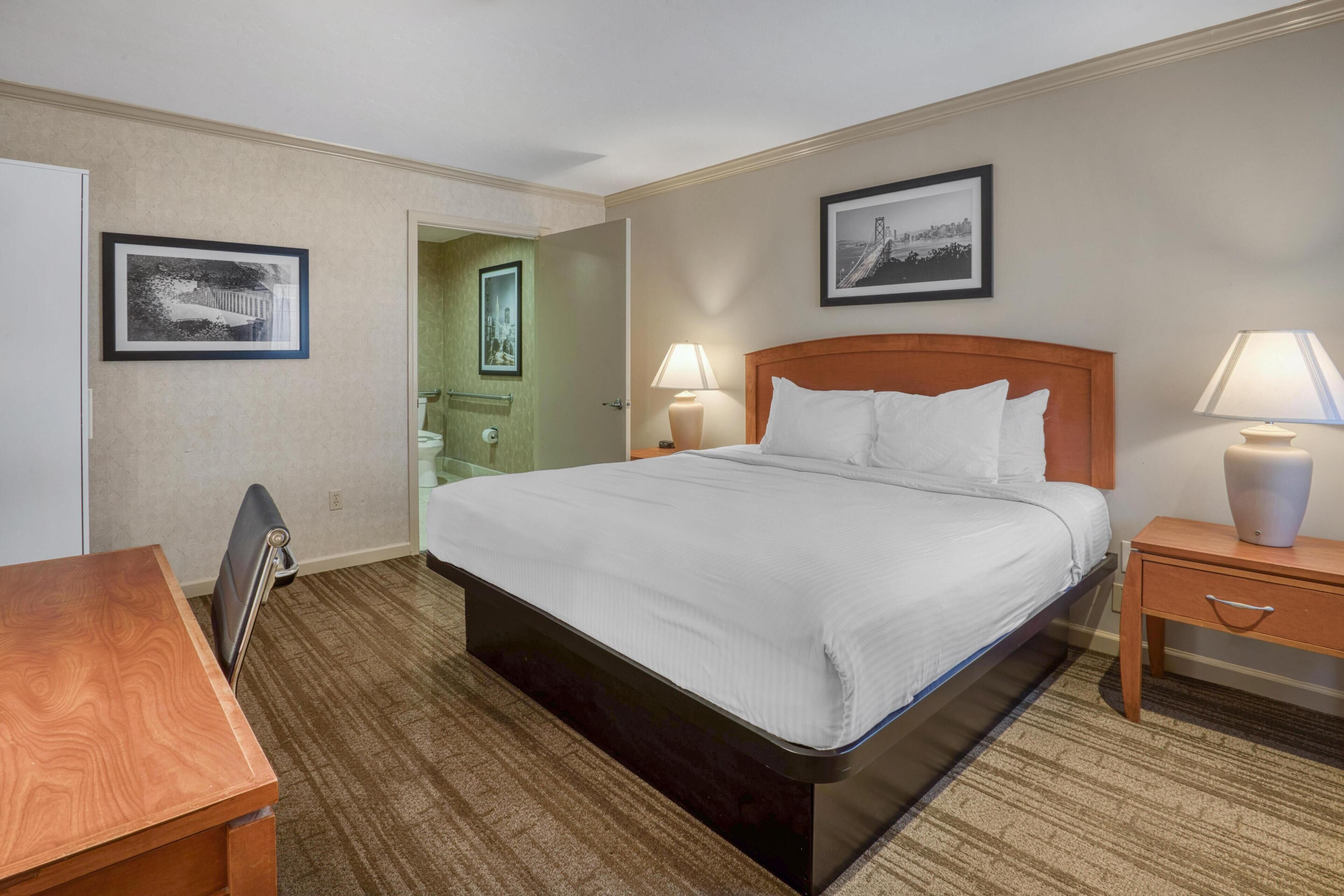 Ein Hotelzimmer mit einem Bett, Nachttischen, einem Schreibtisch und gerahmten Bildern an den Wänden.