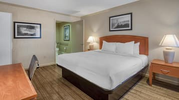 Una habitación de hotel con cama, mesitas de noche, un escritorio y cuadros en las paredes.