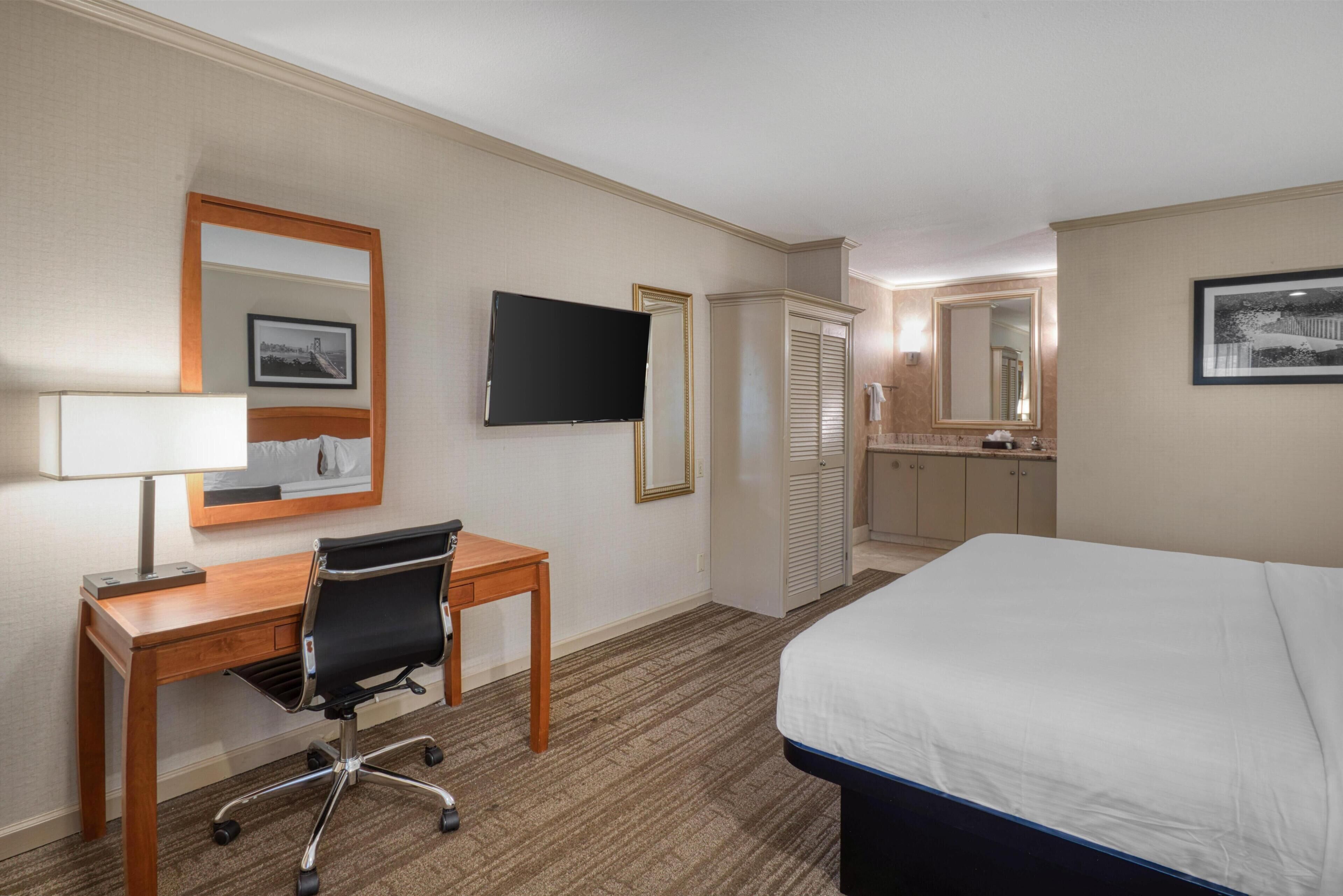 Une chambre d’hôtel comprenant un lit, un bureau, une chaise, une télévision, une armoire et une salle de bain.