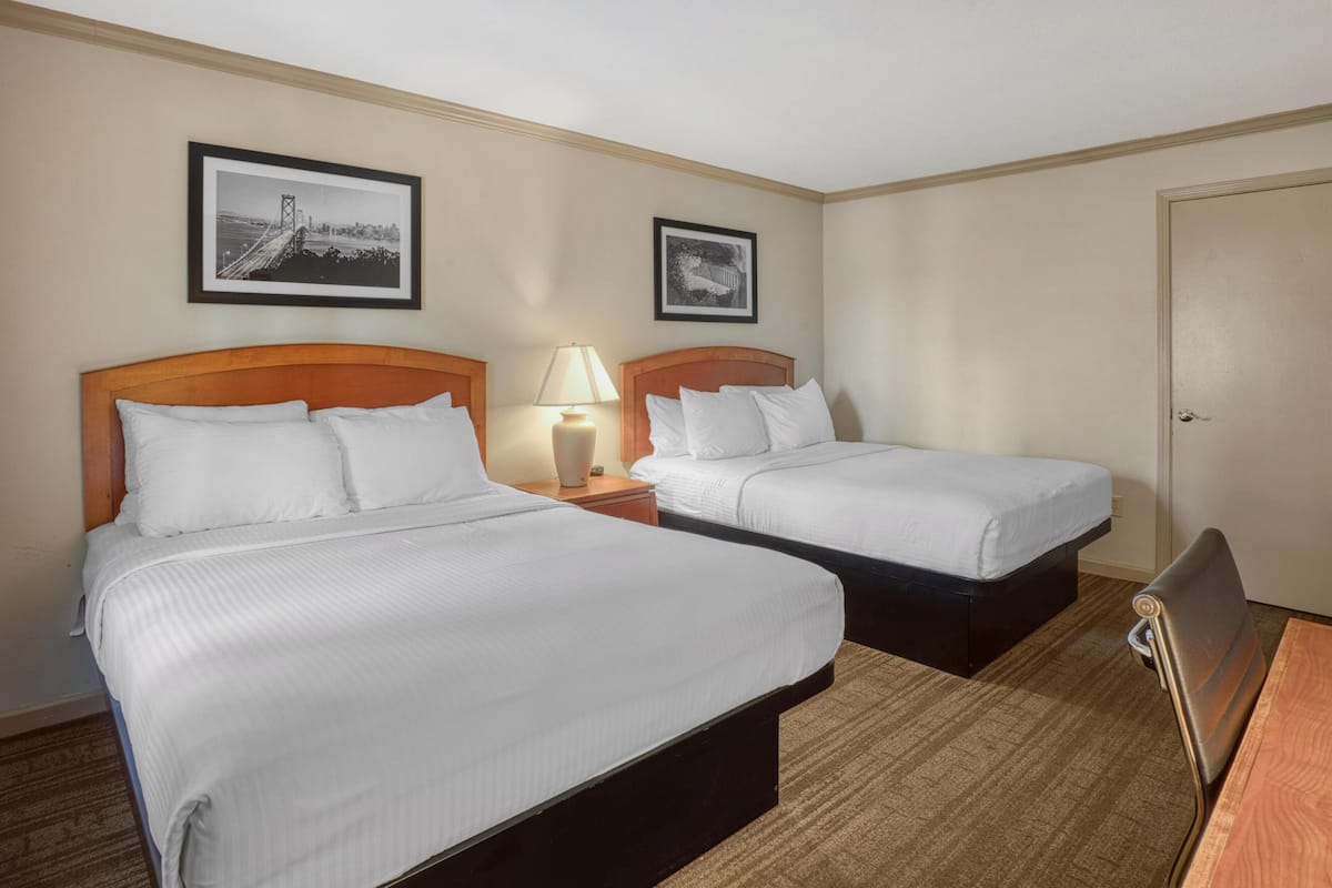 A hotel room with two beds, a nightstand with a lamp, and two framed pictures on the wall.