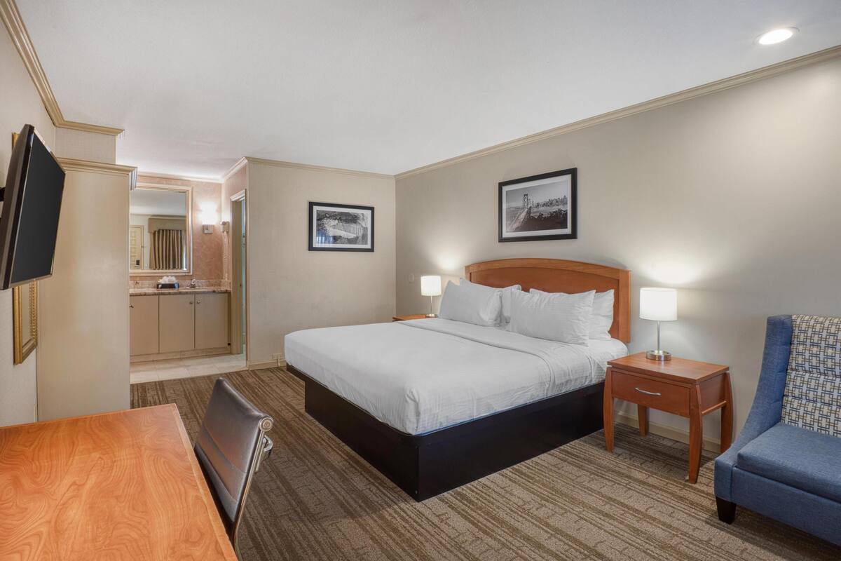 A hotel room with a bed, bedside tables, a TV, a desk, and a chair.