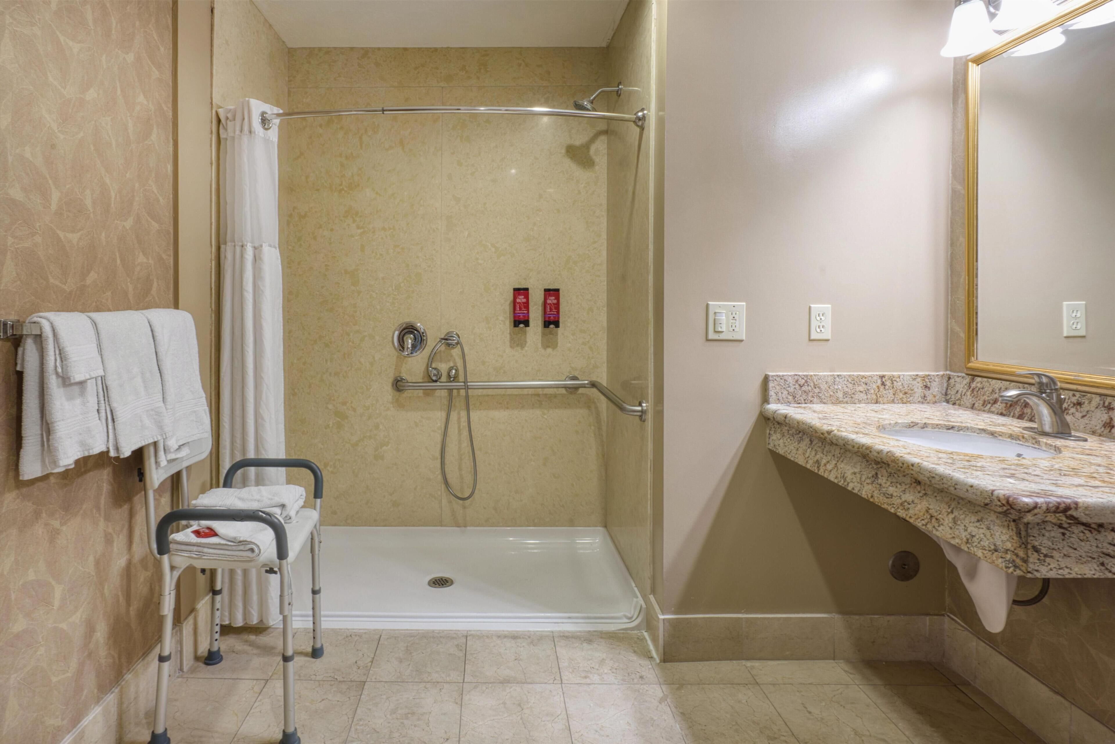 A bathroom with a shower, grab bar, and a sink with a marble countertop.