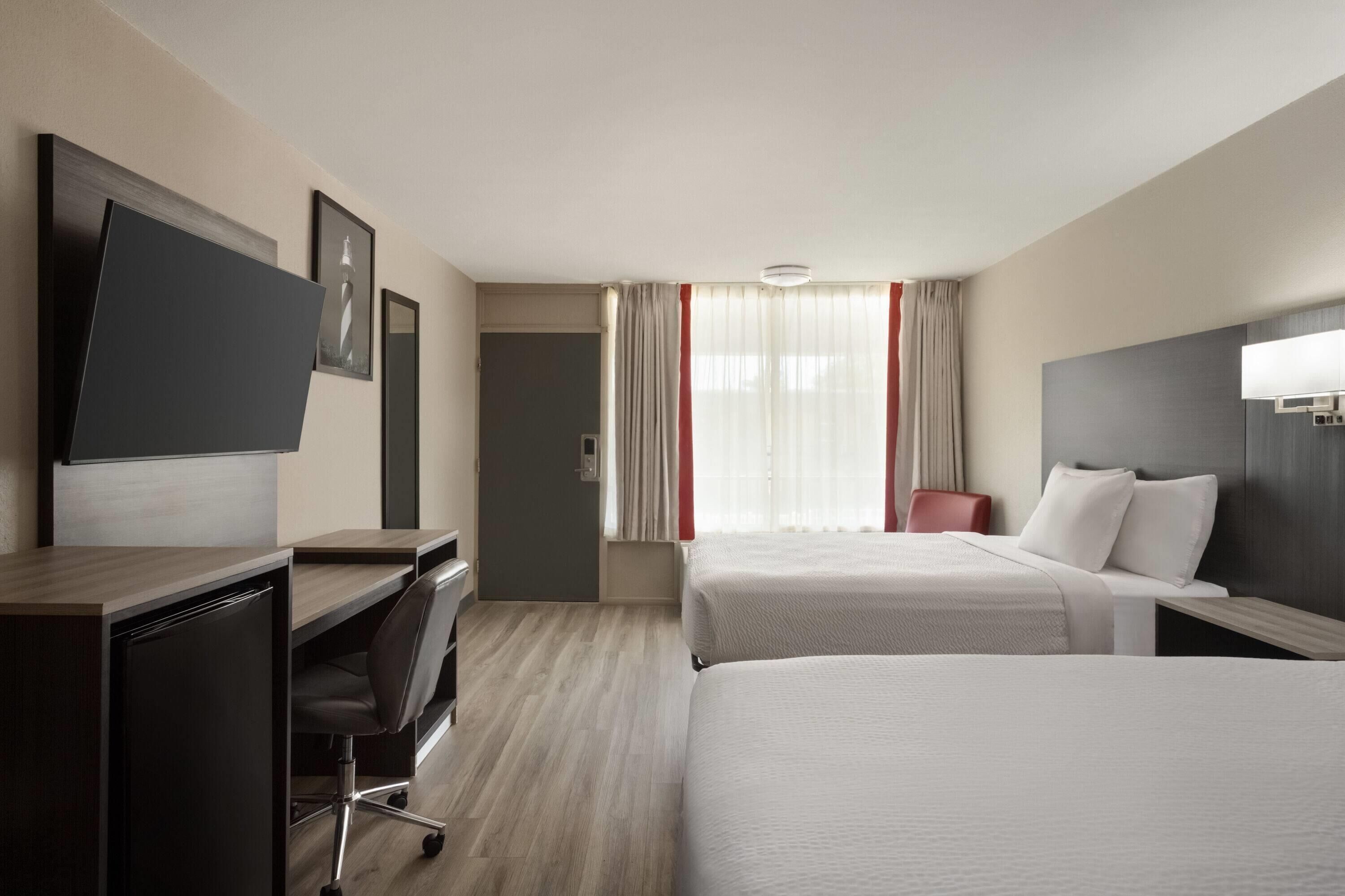 A hotel room with two beds, a desk, a chair, a TV, and a window with curtains.