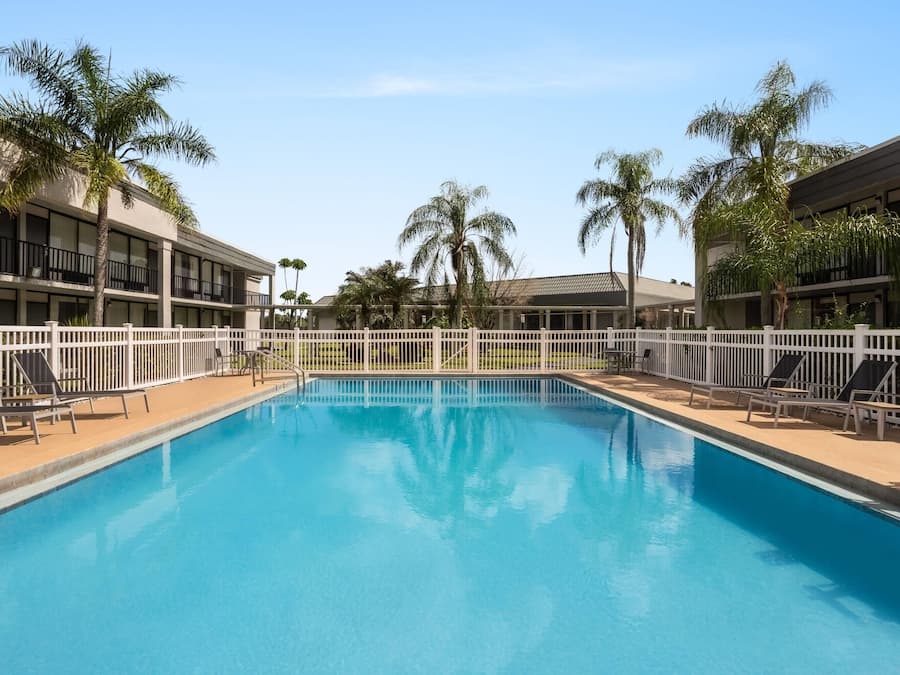 A swimming pool with a white fence, lounge chairs, and palm trees.