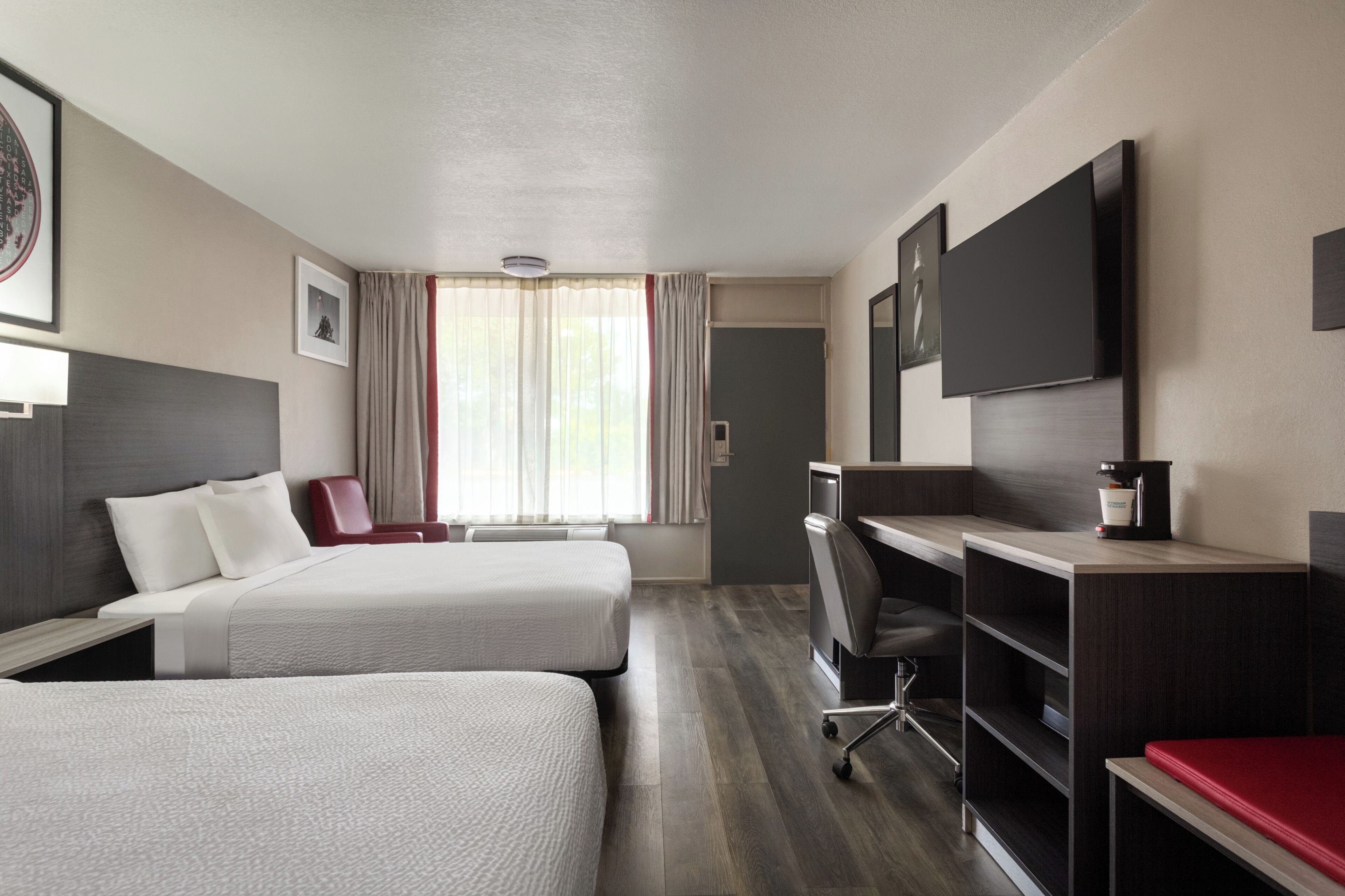 A hotel room with two beds, a desk, a chair, a flat-screen TV, and a coffee machine.