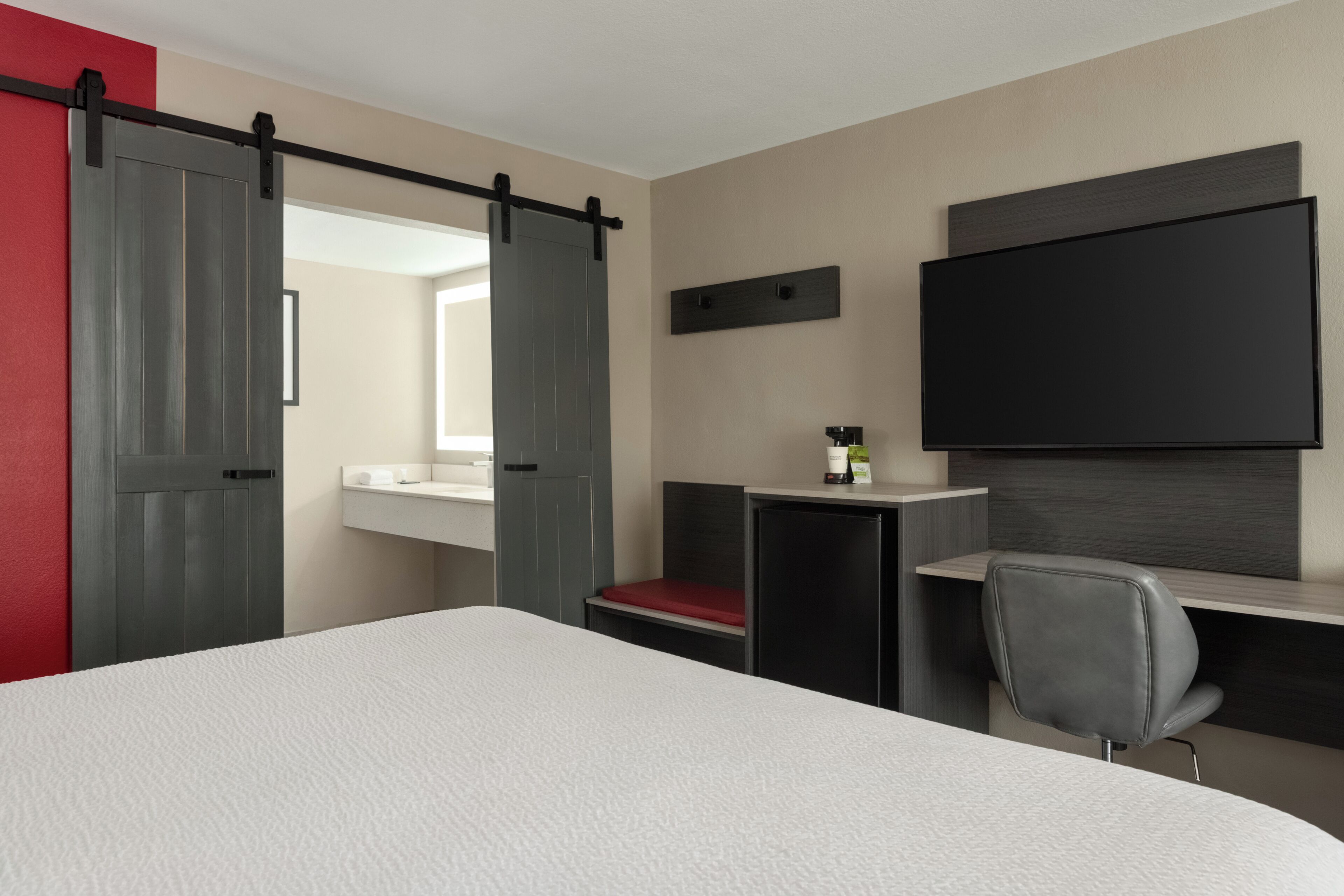 Habitación de hotel con cama, escritorio, silla, televisor y puerta corrediza.