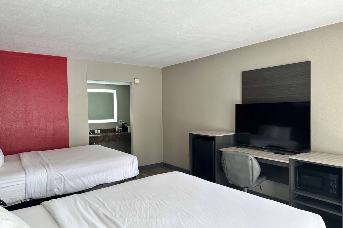 A hotel room with two beds, a TV, a desk with a computer, and a microwave.
