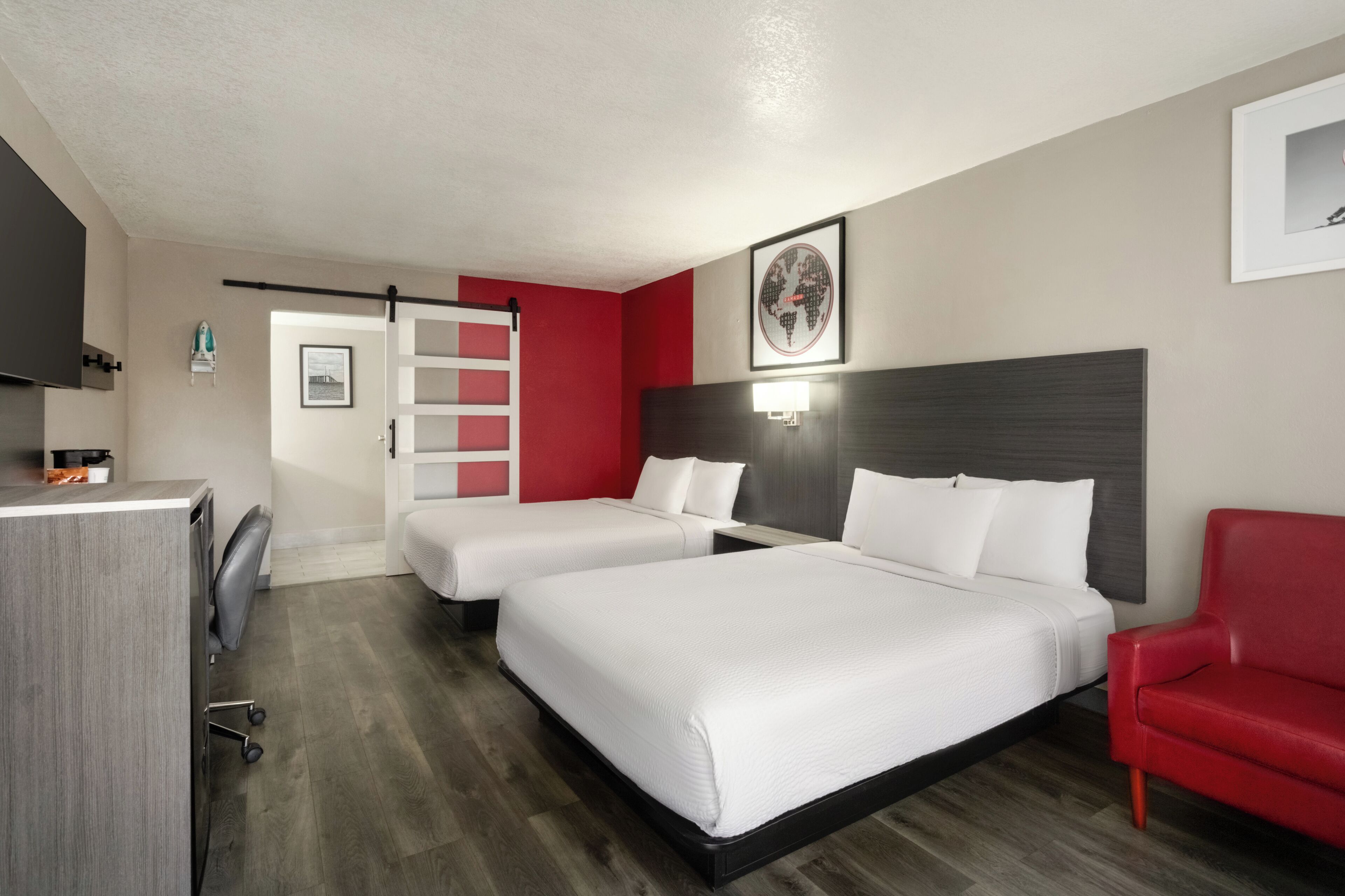 A hotel room with two beds, a red chair, a desk, and a world map on the wall.