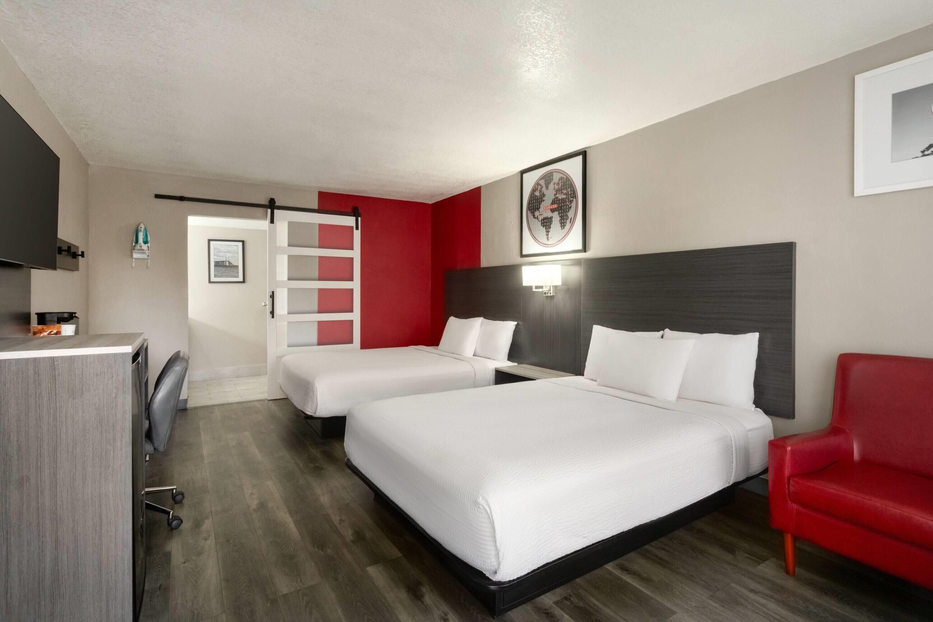 Una habitación de hotel con dos camas, un escritorio, una silla roja y un mapa mundial en la pared.
