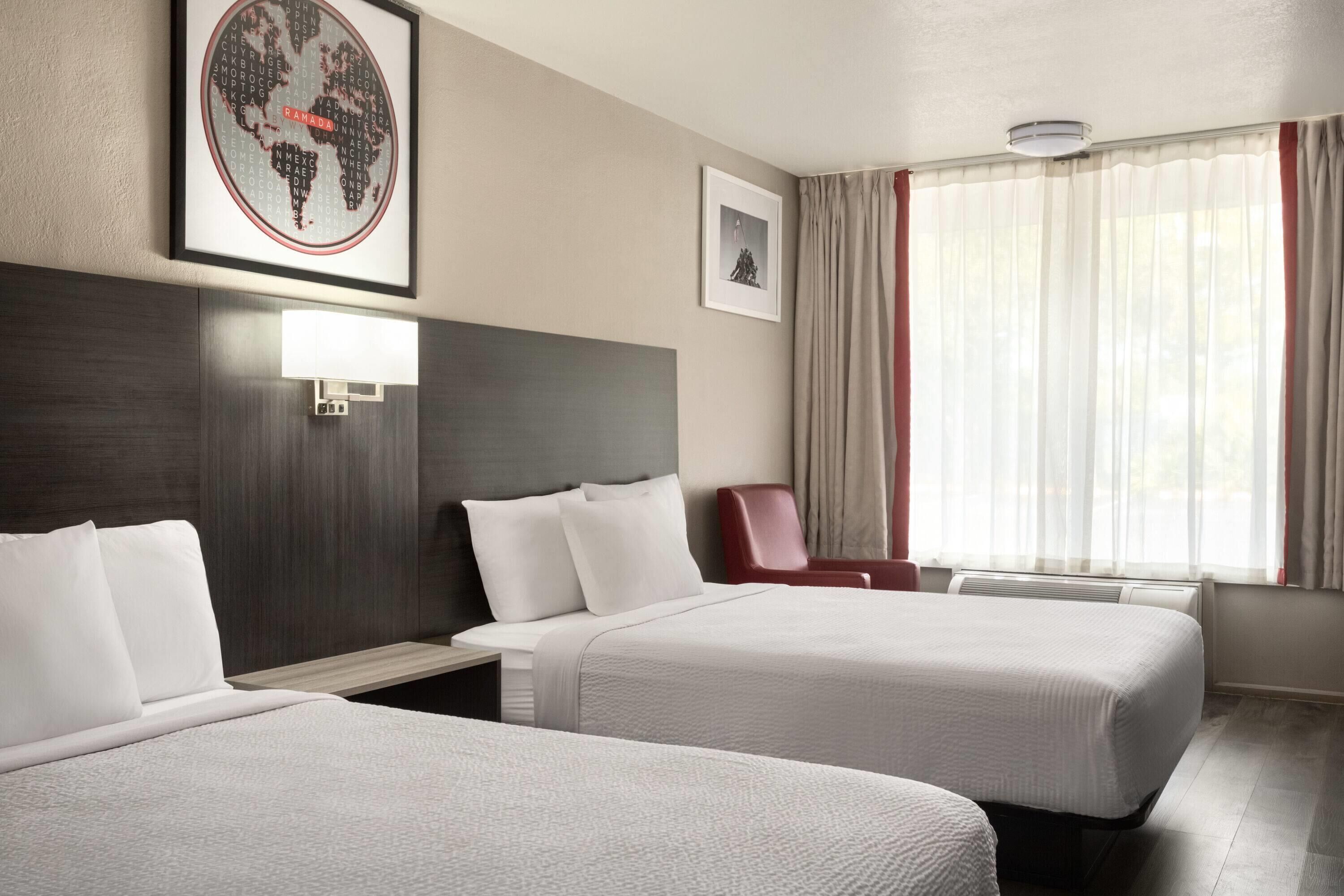 A hotel room with two beds, a desk, a chair, a framed world map, and a framed picture on the wall.