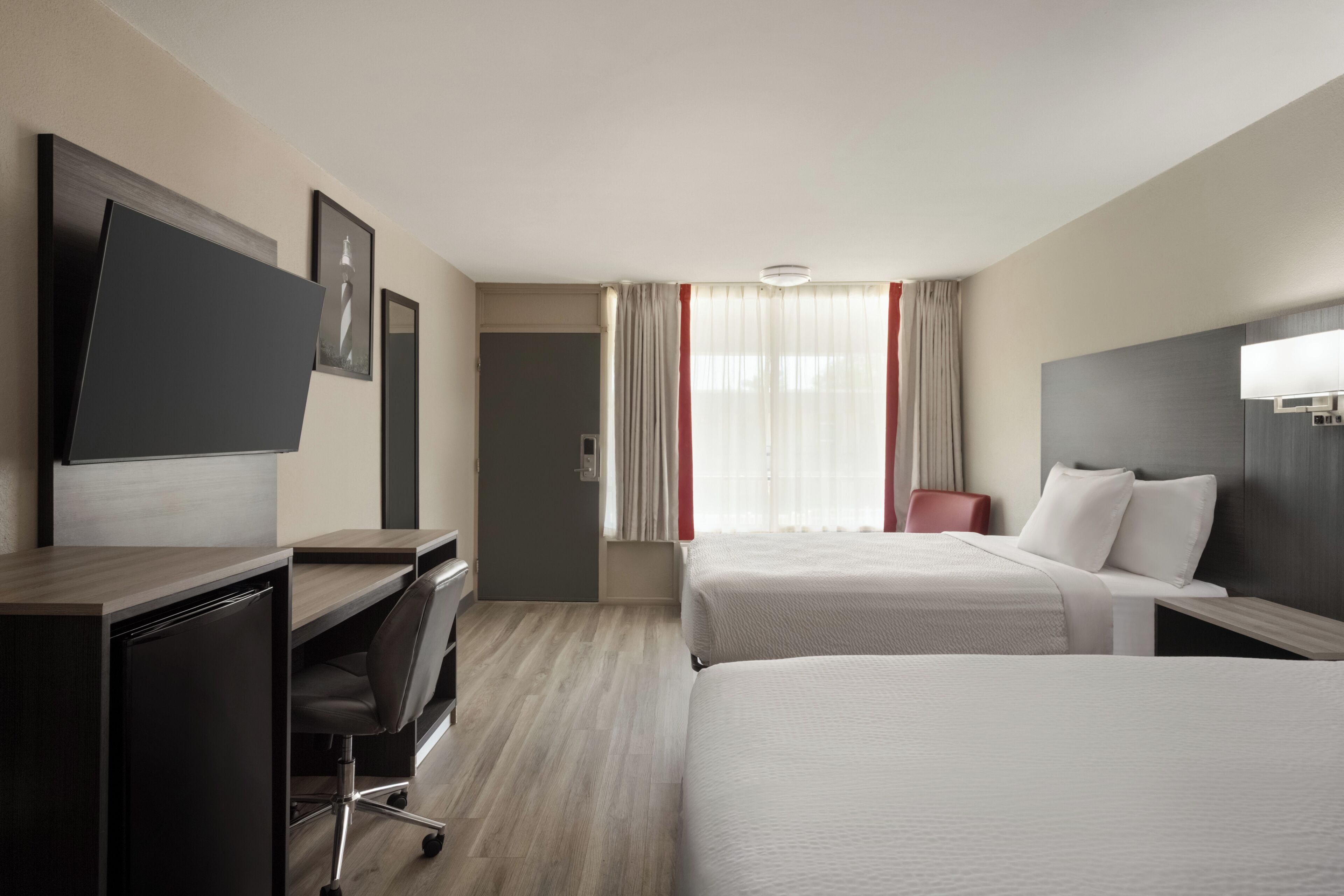 A hotel room with a bed, a desk, a chair, a television, and a window with curtains.