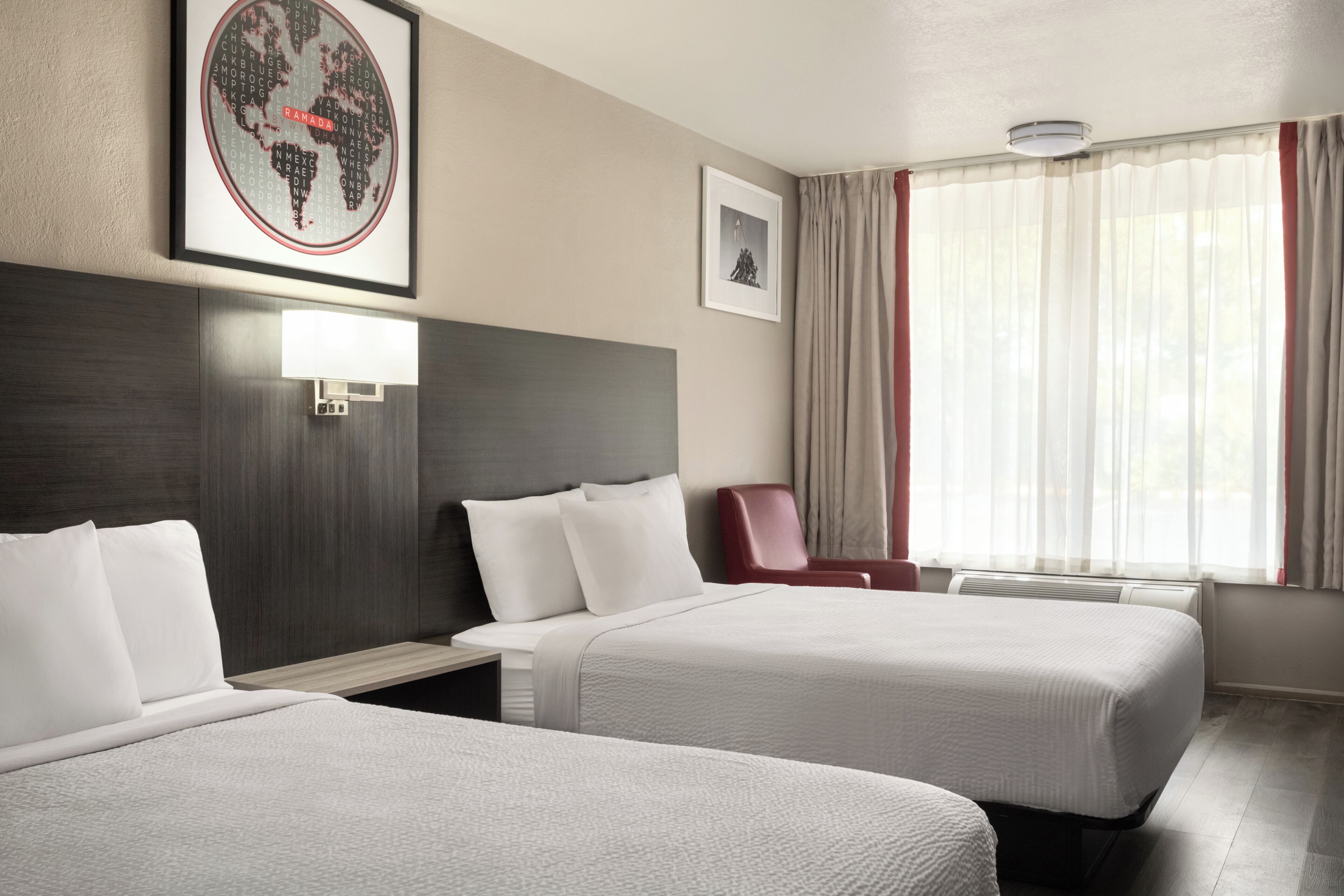 Ein Hotelzimmer mit zwei Betten, einem Schreibtisch, einem Stuhl, einem Wandbild mit einer Weltkarte und einem gerahmten Bild an der Wand.