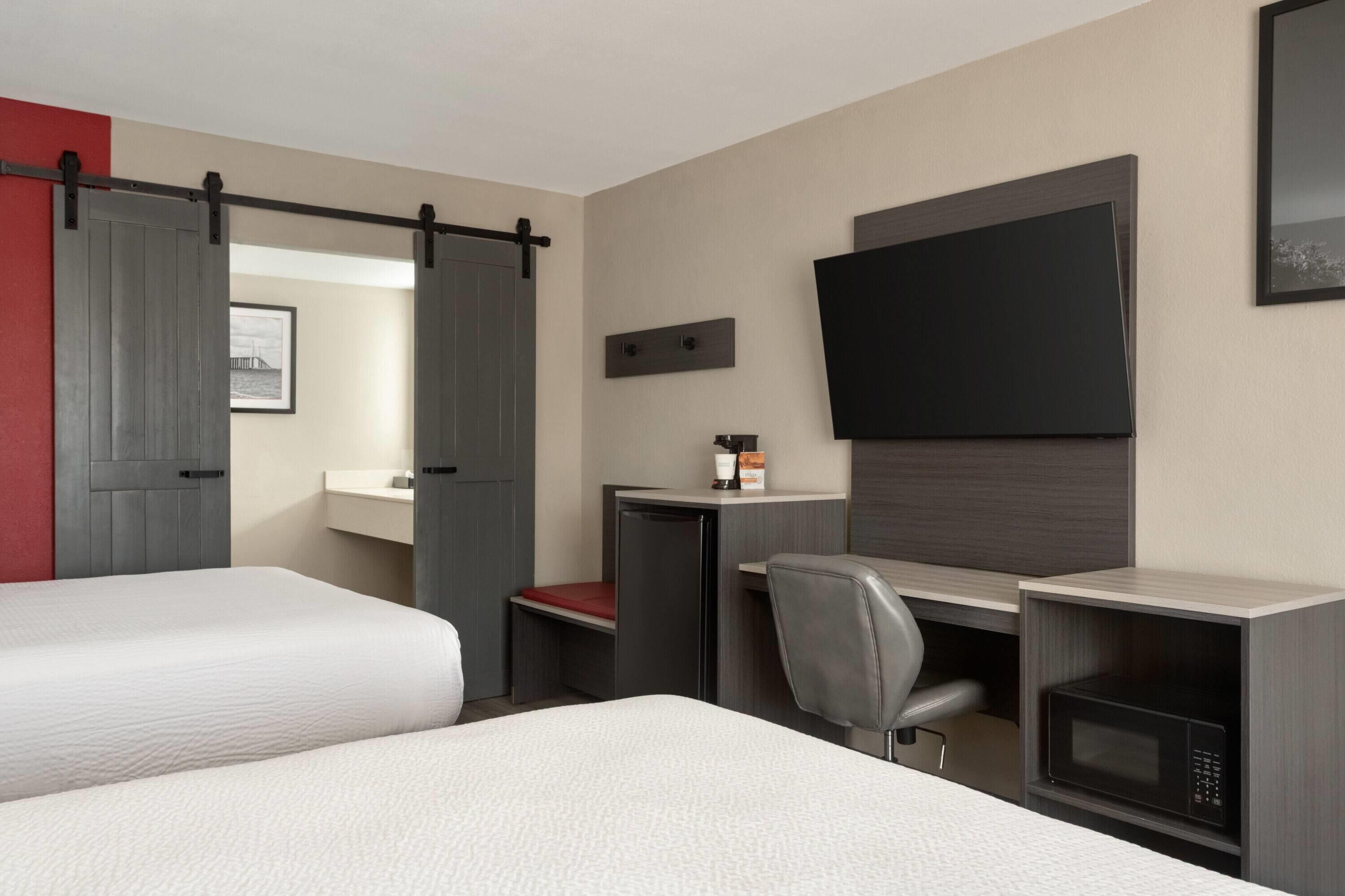 Habitación de hotel con dos camas, un escritorio, una silla, un televisor y un microondas.