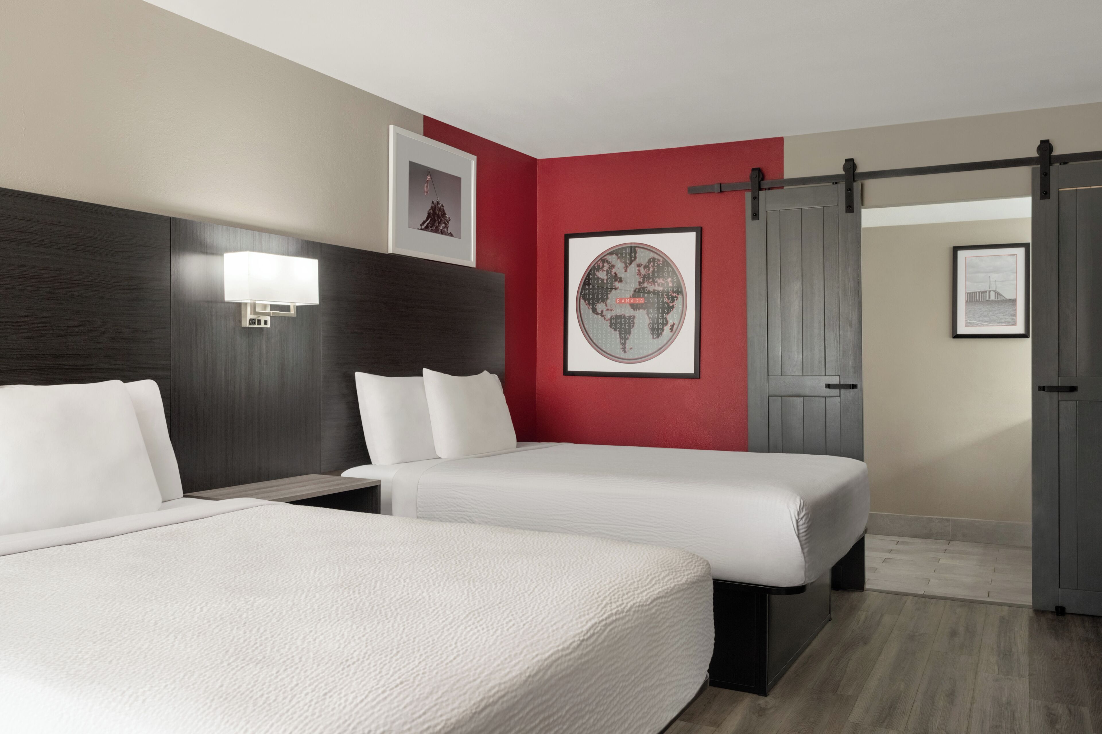 A hotel room with two beds, a large wall-mounted fan, and a door with a sliding mechanism.