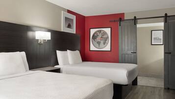 A hotel room with two beds, a large wall-mounted fan, and a door with a sliding mechanism.