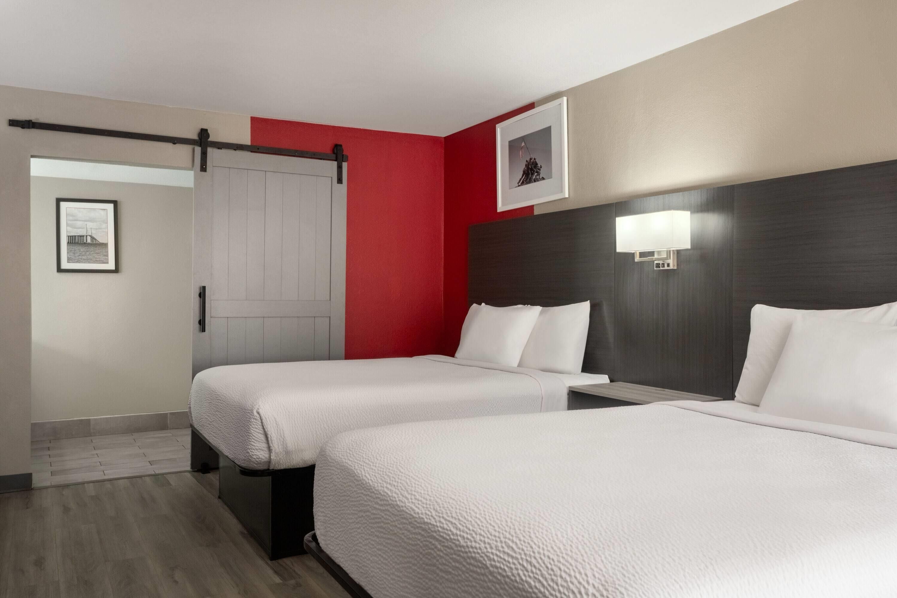 A hotel room with two beds, a sliding door, a framed picture on the wall, and a bedside lamp.